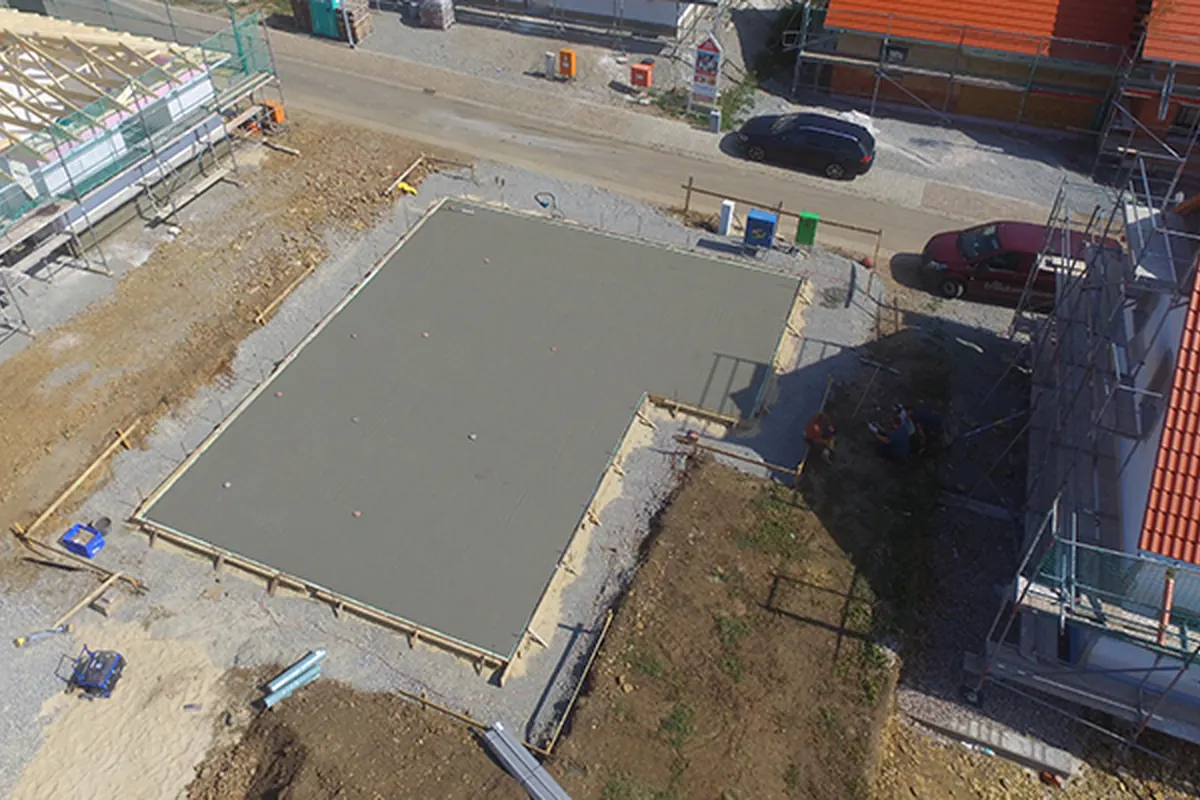 Fertige Betonbodenplatte des Bungalows auf der Baustelle – Luftaufnahme mit Baugerüst der Nachbargebäude