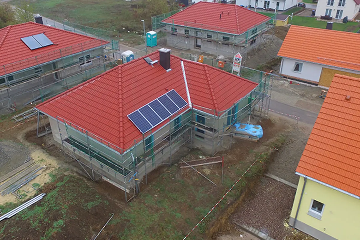 Bungalow mit rotem Walmdach und Photovoltaikanlage nach dem Grundputz, eingerüstet – Luftaufnahme im Herbst