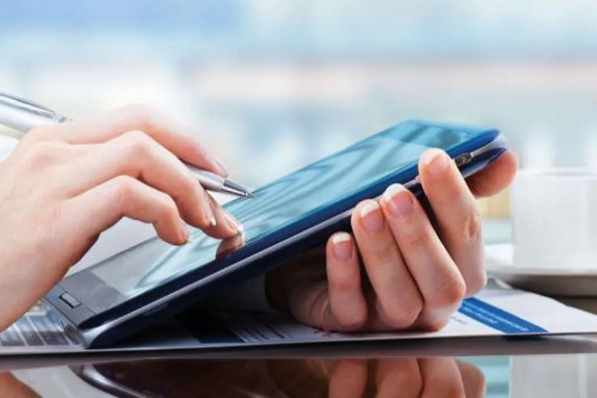Hände mit Stift und Tablet über Unterlagen am Schreibtisch